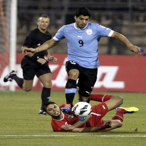 Photo: Uruguay star Luis Suarez dribbles past Jordan midfielder Saeed Al-Murjan (bottom) during their FIFA Play Off match in November 2013. (Copyright AFP 2014: Khalil Mazraawi)