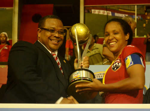 Photo: Trinidad and Tobago captain Maylee Attin-Johnson (right) collects the 2014 Caribbean Cup trophy from CFU president Gordon Derrick. (Courtesy Jinelle James/WOLF)