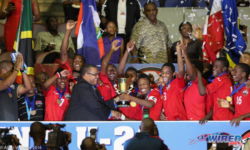 Photo: Trinidad and Tobago National Under-20 captain Shannon Gomez (centre) takes the 2014 Caribbean Cup trophy from CFU president Gordon Derrick. (Courtesy Allan V Crane/Wired868)