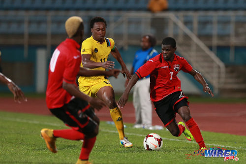 Photo: Trinidad and Tobago midfielder Hughtun Hector (right) advances while Antigua and Barbuda defender Quinton Griffith (centre) and Kevin Molino watch on during the 2014 Caribbean Cup qualifying round. (Courtesy Allan V Crane/Wired868)