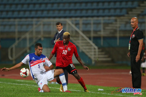 Photo: Trinidad and Tobago midfield ace Kevin Molino (centre) flicks the ball around Dominican Republic midfielder Heinz Barmettler (left) during the 2014 Caribbean Cup qualifiers while coach Stephen Hart looks on. (Courtesy Allan V Crane/Wired868)