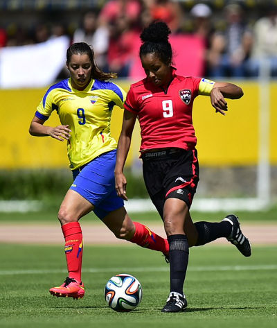 Photo: Trinidad and Tobago midfielder and captain Maylee Attin-Johnson (right) advances with the ball under pressure Ecuador star Gianina Lattanzio during the first leg of the 2015 FIFA Play Off in Quito. (Copyright AFP 2014/Rodrigo Buendia)