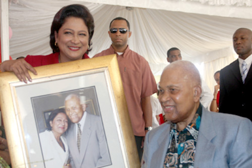 Photo: Prime Minister Kamla Persad-Bissessar (left) presents a framed photograph to her former Cabinet colleague and late Prime Minister ANR Robinson. (Courtesy Gov.tt)