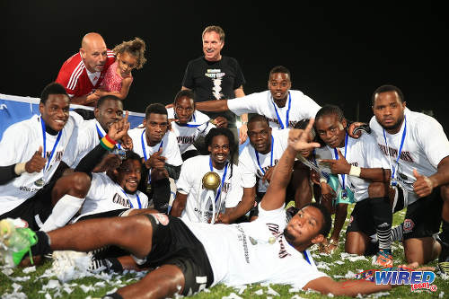 Photo: Central FC goal scorer Jean-Luc Rochford (front) and his teammates celebrate with the 2015 Caribbean Club Championship trophy. Looking on is Central FC operations director Kevin Harrison (top left) and Bankers Insurance CEO Vance Gabriel (top centre). (Courtesy Allan V Crane/Wired868)