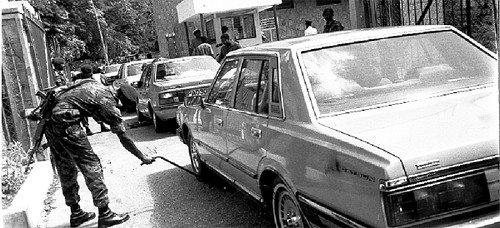 Photo: A soldier searches for a car bomb in the immediate aftermath of the July 27 attempted coup in Port of Spain. (Copyright Trinidad Guardian)