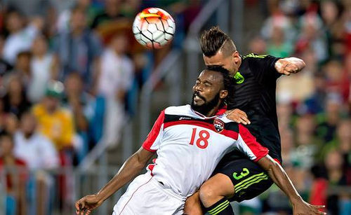 Photo Trinidad and Tobago defender Yohance Marshall (left) wins a header from Mexico defender Yasser Corona in CONCACAF 2015 Gold Cup action. (Courtesy CONCACAF)