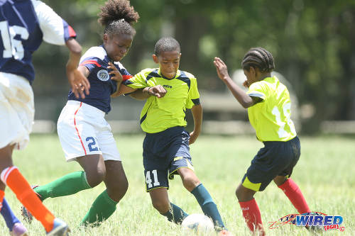 Photo: Trendsetter Hawks Under-11 midfielder Josiah Wilson (centre) tries to shake off attention from a Santa Cruz FA player (left) during 2015 Republic Bank National Youth Cup Under-13 action at the Queen's Park Savannah. (Courtesy Allan V Crane/Wired868)