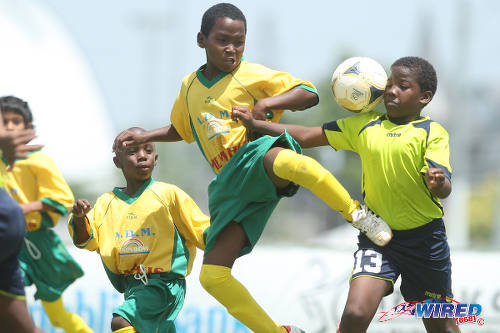 Photo: A Memphis FC player (centre) gives the boot to a Trendsetter Hawks opponent during North Zone Under-11 action at the 2015 Republic Bank Youth Cup in the Queen's Park Savannah.  (Courtesy Allan V Crane/Wired868)