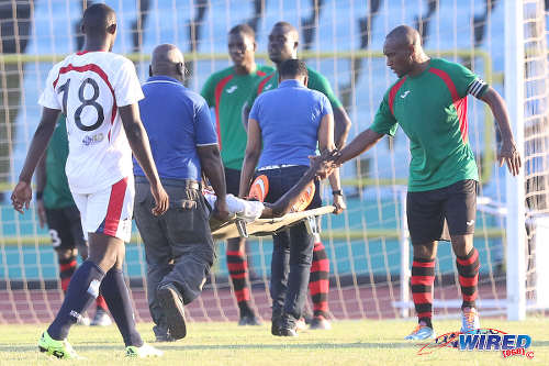 Photo: San Juan Jabloteh captain Damian Williams (right) offers a hand to Morvant Caledonia United player Sheldon Holder as he is stretchered off during 2015/16 Pro League action. (Courtesy Chevaughn Christopher/Wired868)