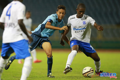 Photo: Naparima College playmaker Shane Sandy (right) tries to wriggle away from a QRC opponent during 2015 SSFL Premier Division action. (Courtesy Allan V Crane/Wired868)