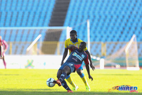 Photo: Morvant Caledonia United midfielder Akeem Roach (foreground) passes the ball while Defence Force midfielder Dave Long looks on in 2015 First Citizens Bank action. (Courtesy Chevaughn Christopher/Wired868)