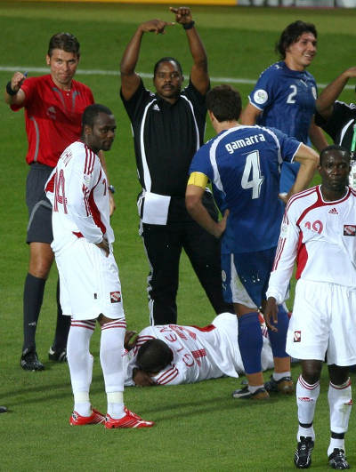 Photo: Strength and conditioning coach Zeph Nicholas (top) motions for a substitution as Trinidad and Tobago attacker Cornell Glen (bottom) lies injured on the ground during 2006 World Cup action against Paraguay. Looking on are captain Dwight Yorke (right) and Stern John. (Copyright AFP 2015)