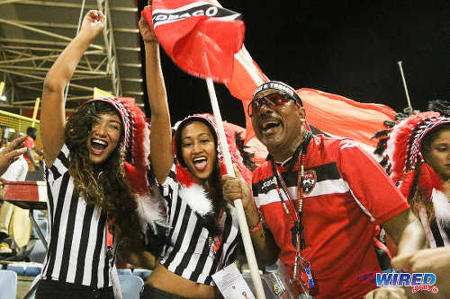 Photo: Soca Warriors supporter Joey "Posh" Richardson (right) exchanges notes with some football fans during 2018 World Cup qualifying action against the United States on 17 November 2015. (Courtesy Chevaughn Christopher/Wired868)