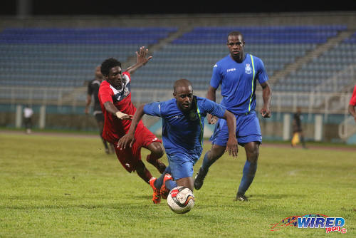 Photo: Police FC defender Dexter Alleyne (centre) tumbles under pressure from Club Sando utility player Akeem Humphrey (left) during 2015/16 Pro League action in Couva. (Courtesy Chevaughn Christopher/Wired868)