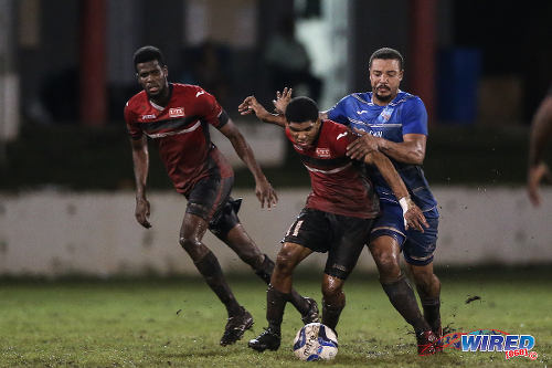 Photo: UTT midfielder Ricaldo Castellano (centre) holds off a QPCC opponent during 2015 CNG NSL Championship Division action at UTT Grounds, Arima. (Courtesy Allan V Crane/CA-images/Wired868)