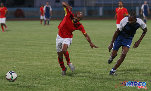 Photo: DJ and soca artiste Jason "JW" Williams (left) tries to keep his balance after a challenge from former World Cup 2006 defender Dennis Lawrence (centre) sets a screen during an exhibition match at the Ato Boldon Stadium in Couva on 10 April 2017. (Courtesy Sean Morrison/Wired868)